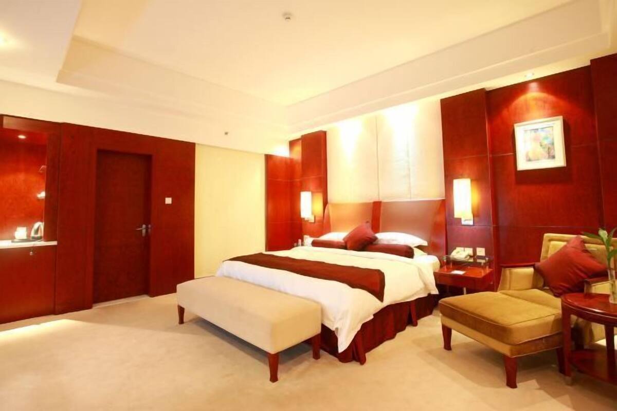 A hotel room with a large bed, a bedside table, a chair, and a desk with a lamp.