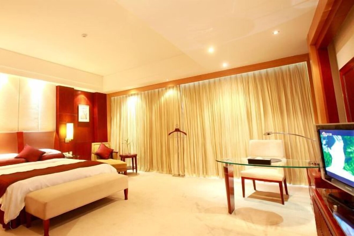 A hotel room with a bed, bedside tables, a TV, and a curtain.
