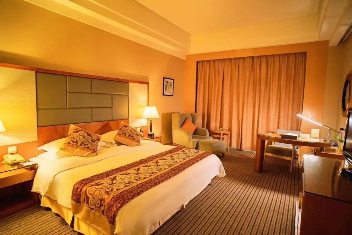 A hotel room with a large bed, a desk, a chair, and a television.