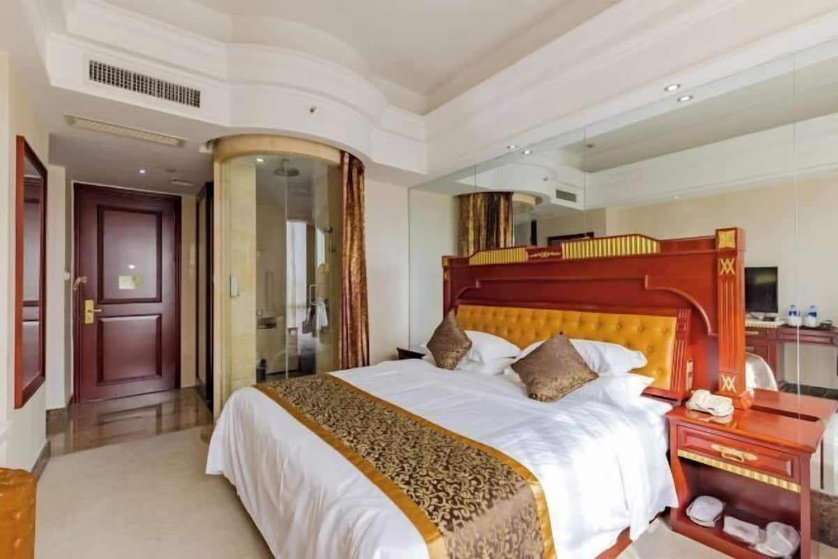 A hotel room with a large bed, a wooden headboard, a bedside table, and a mirror.