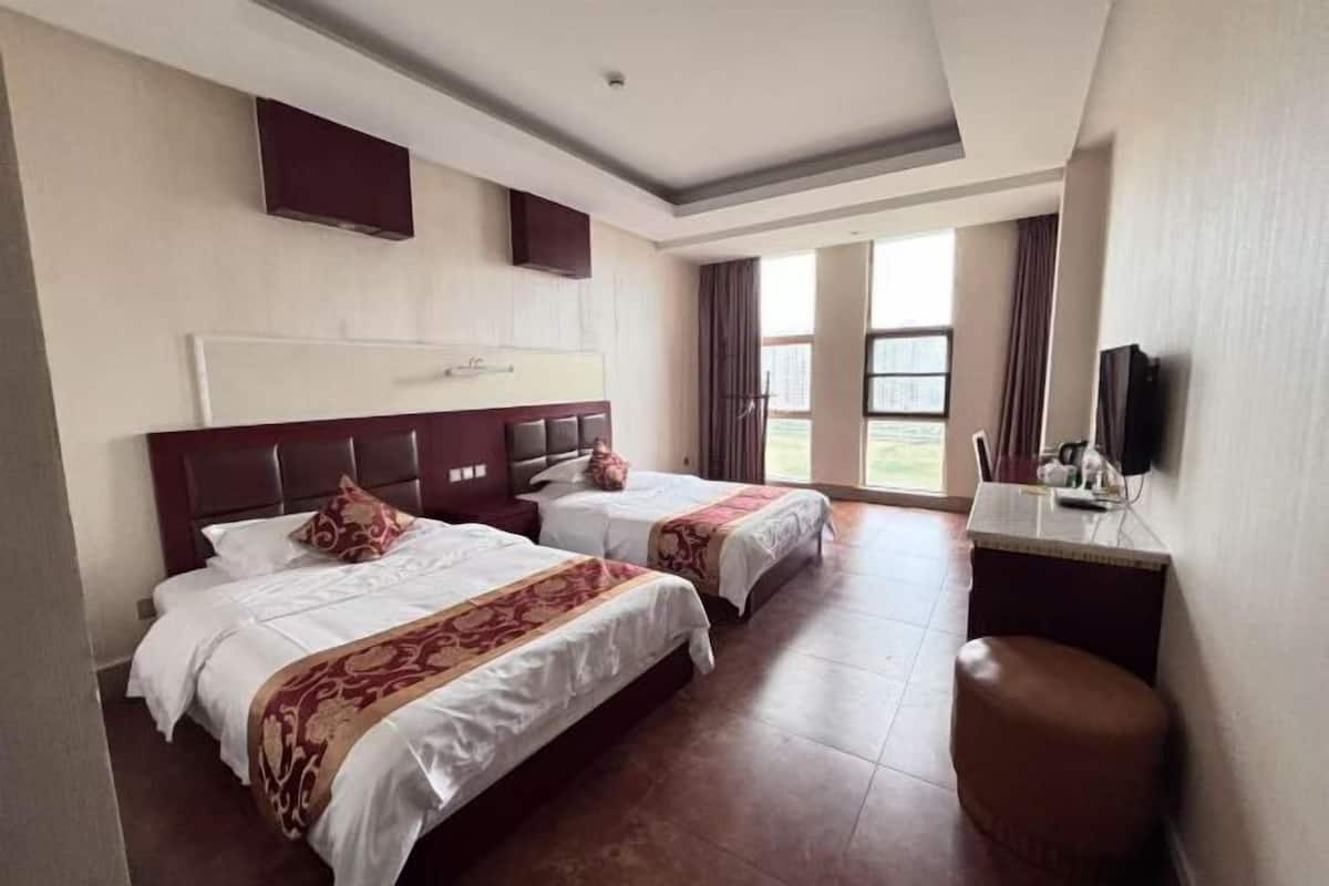 A hotel room with two beds, a television, and a view of the outdoors.