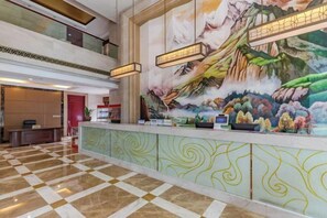 A hotel reception area with a check-in counter, a large mural, and a check-in machine. - Fan Chang Hotel (Wuhu)