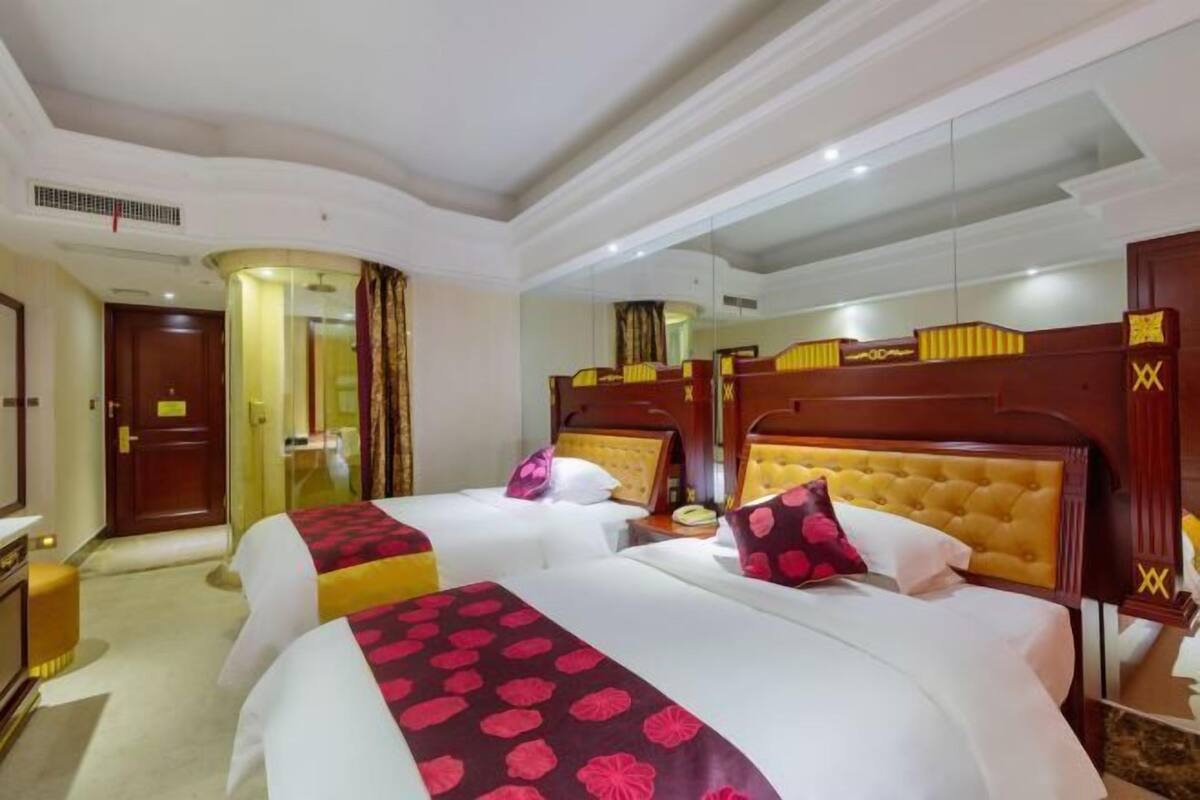 A hotel room with two beds, a large mirror, and a wooden headboard.