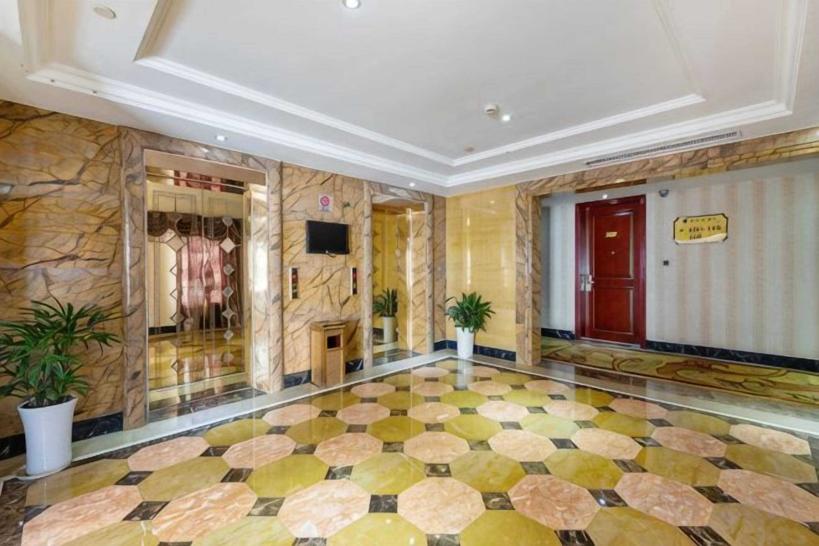 Un vestíbulo de hotel con piso de mármol, una recepción y una puerta roja.