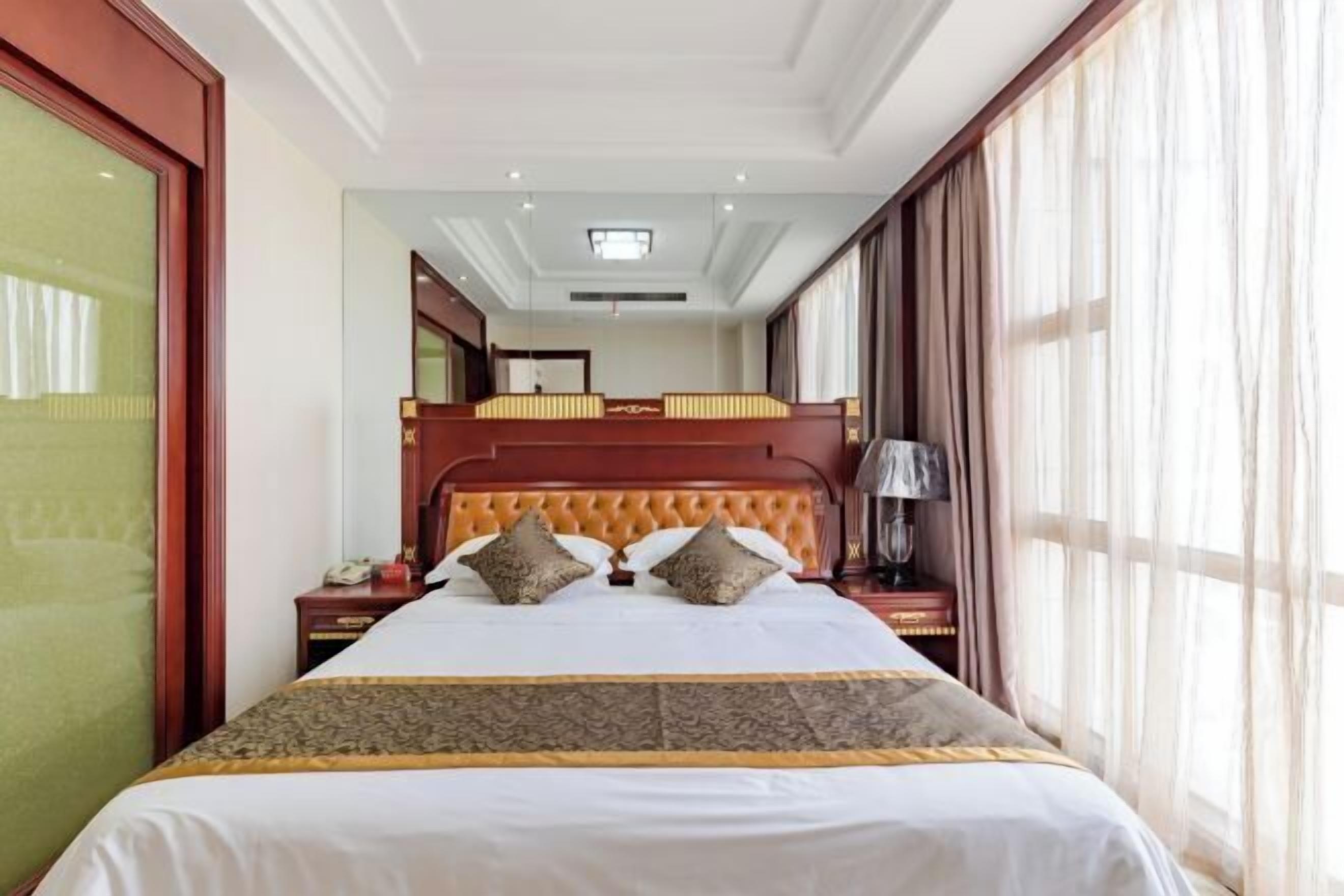Une chambre d’hôtel avec un grand lit, un bureau, une chaise, une lampe et une fenêtre avec des rideaux.