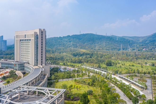 Un edificio moderno con fachada de vidrio curvo, rodeado de un paisaje verde y una autopista.