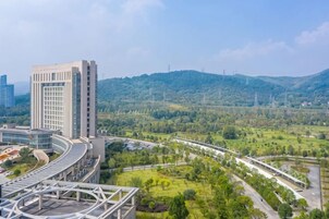 Un edificio moderno con fachada de vidrio curvo, rodeado de un paisaje verde y una autopista.