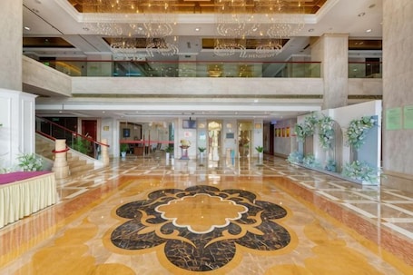 A spacious lobby with a grand chandelier, a central floral floor design, and a staircase leading to an upper level.. Fan Chang Hotel
