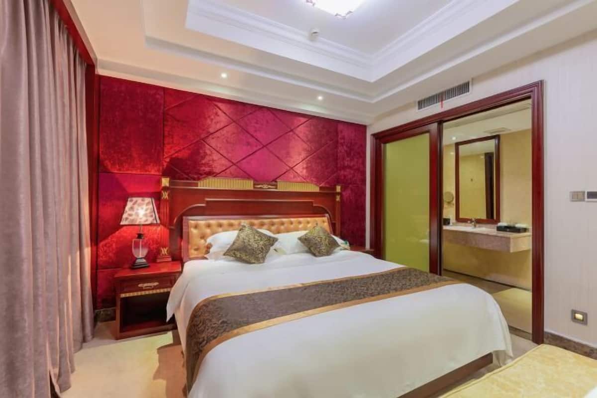 A hotel room with a large bed, a nightstand, a lamp, a mirror, and a wardrobe.