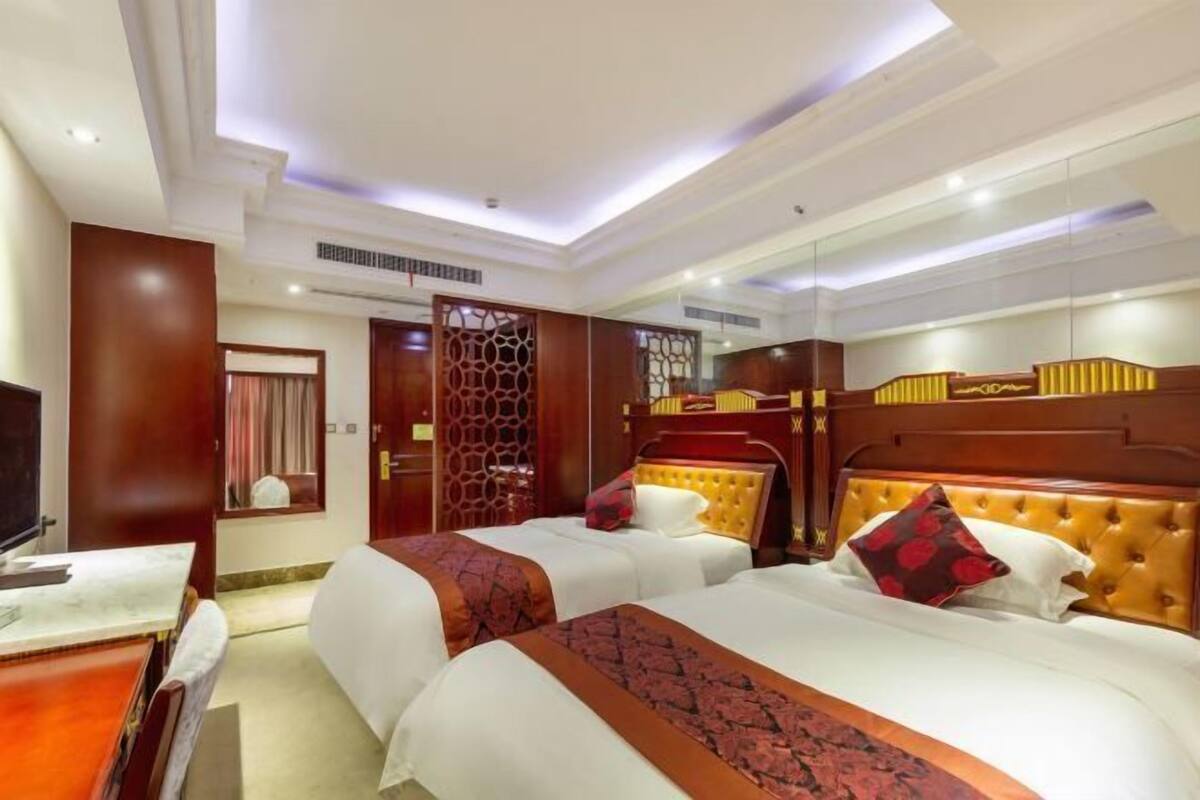 A hotel room with two beds, a TV, a desk, and a mirror.