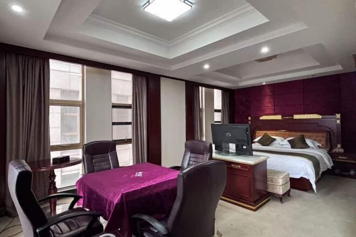 A hotel room with a desk, two chairs, a bed, and a television.