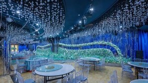 A spacious indoor venue with multiple round tables and chairs, a central floral arrangement, and hanging decorations. - Fan Chang Hotel (Wuhu)