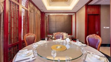 A round table with a glass top, surrounded by chairs, in a room with traditional decor and a large window.
