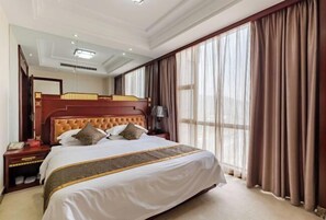 A large bed with a wooden headboard, a bedside table with a lamp, and a large window with curtains. - Fan Chang Hotel (Wuhu)