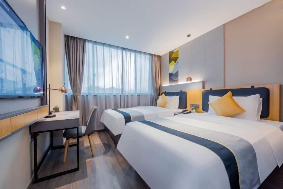 A hotel room with two beds, a desk, and a large window with curtains.