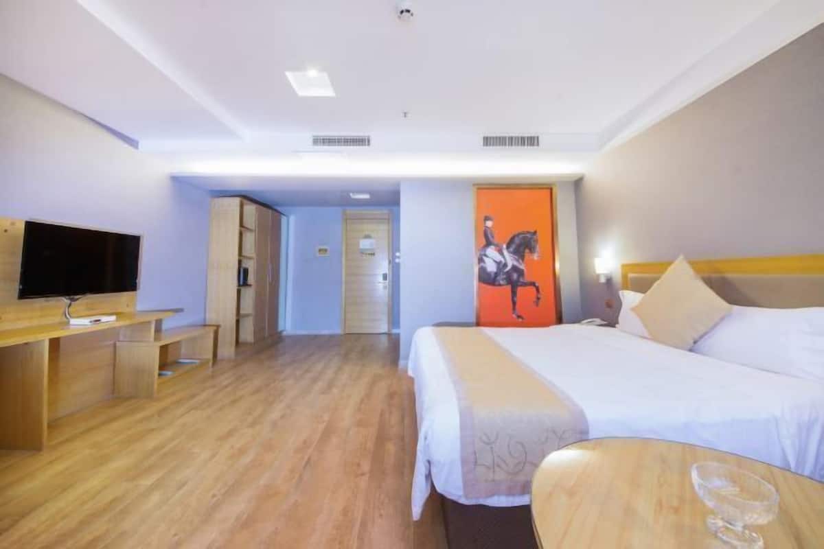 A hotel room with a bed, a desk with a television, a wooden bench, and a door with an orange wall.