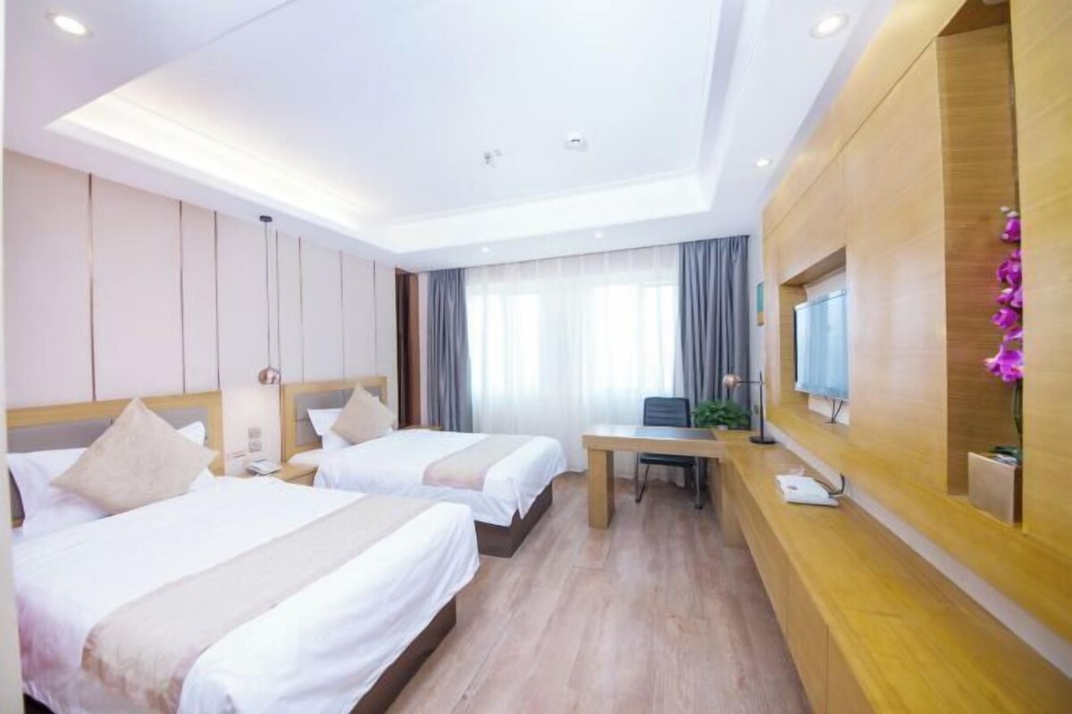 A hotel room with two beds, a desk, a TV, and a wooden reception desk.
