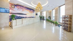 A hotel lobby with a reception desk, a mural, potted plants, and a chandelier. - Jiatai Chain Business Hotel (Zhuanghe High-speed Railway Station) (Zhuanghe)