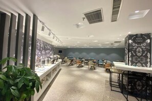A room with multiple tables and chairs, a long counter, and a patterned wall. - Jiatai Chain Business Hotel (Zhuanghe High-speed Railway Station) (Zhuanghe)