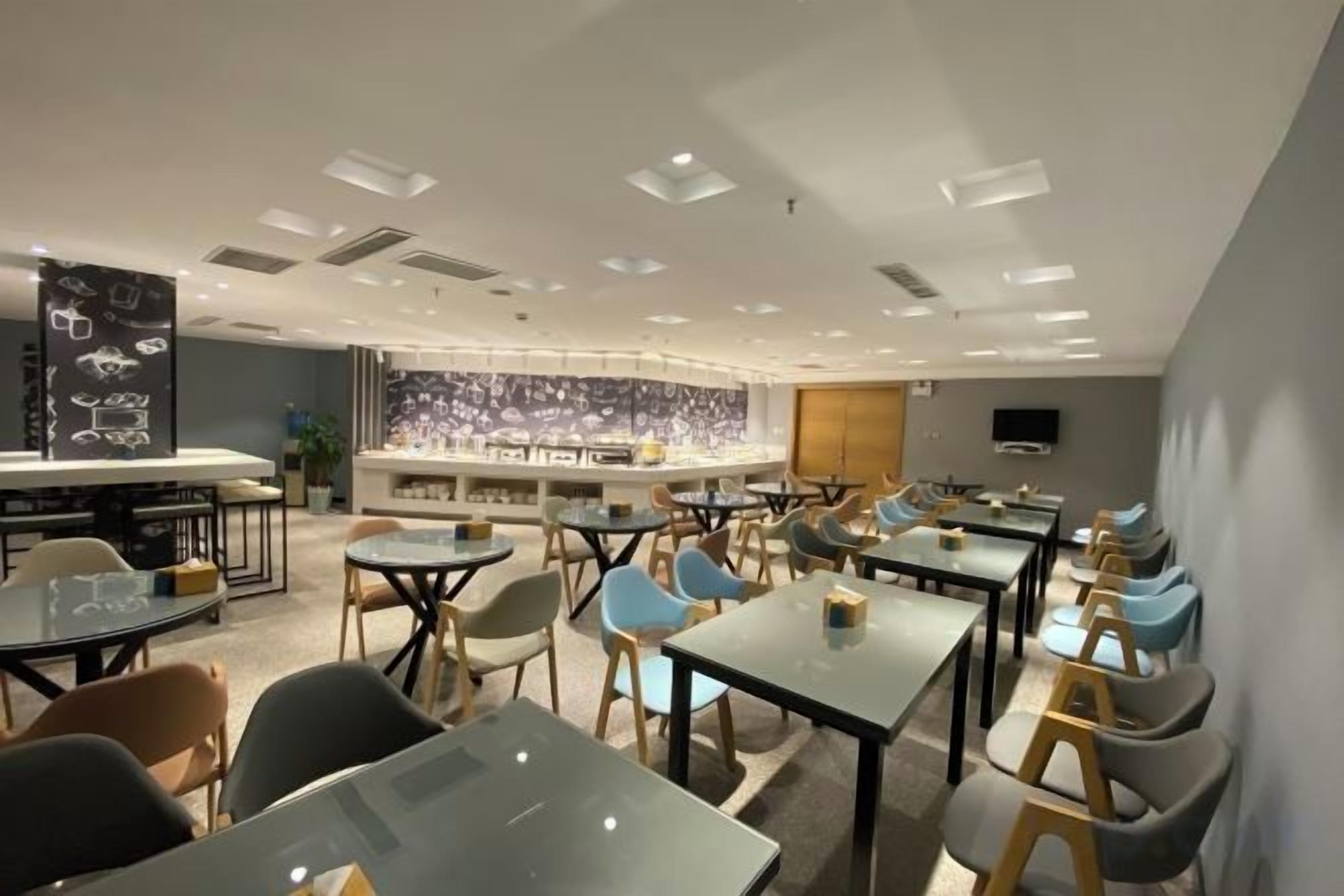 A modern restaurant with multiple tables and chairs, a bar area, and a decorative wall.