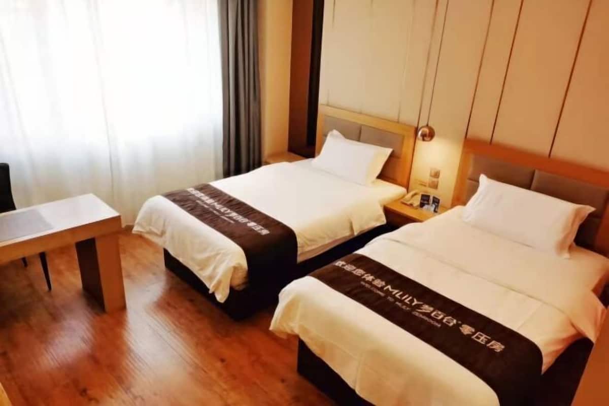 A hotel room with two beds, a wooden floor, a bedside table, and a window with curtains.