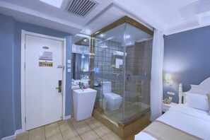 A hotel room with a glass-enclosed shower, a white sink, a toilet, and a bed with white bedding. - Jiatai Chain Business Hotel (Zhuanghe High-speed Railway Station) (Zhuanghe)