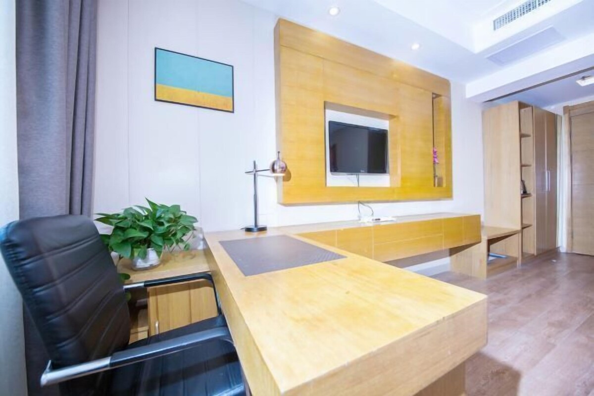 A modern office with a wooden reception desk, a black leather chair, a potted plant, and a mounted TV.