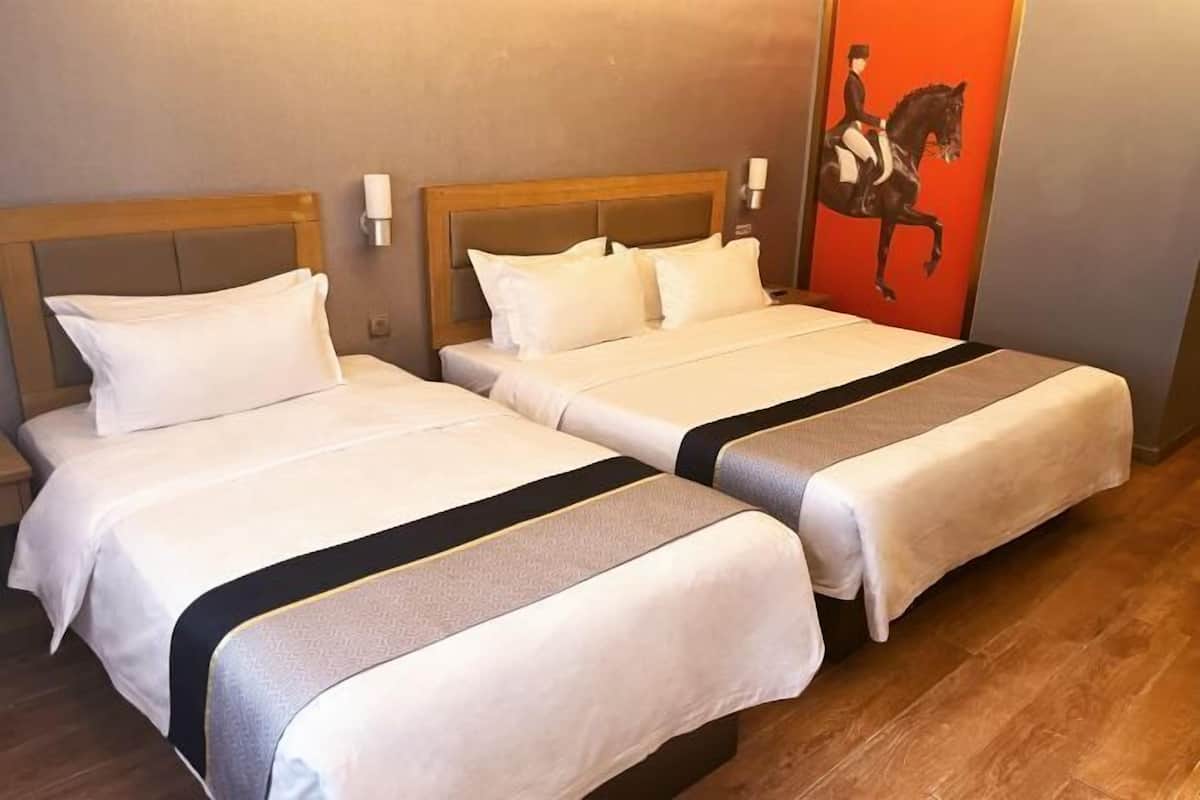 A hotel room with two beds, each with a wooden headboard and white bedding. There is a painting of a horse on the wall.