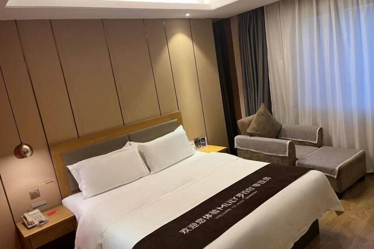 A hotel room with a large bed, a bedside table with a phone, a chair, and a curtain.