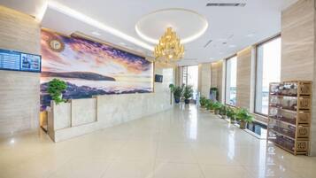 A hotel lobby with a reception desk, a large mural, a chandelier, and a plant display.