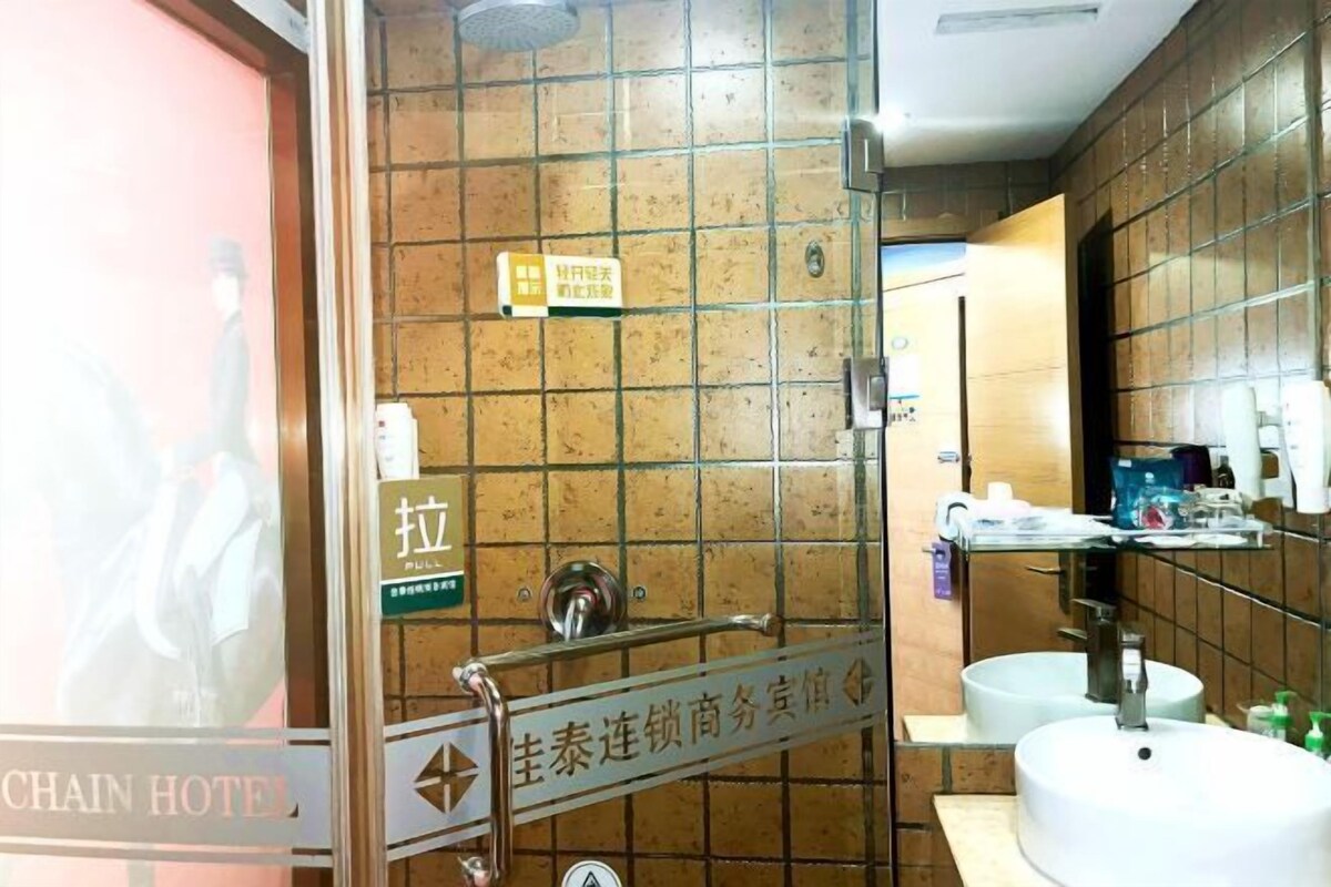 A hotel bathroom with a tiled wall, a sink, and a mirror. There is a sign with Chinese characters and a pull handle.