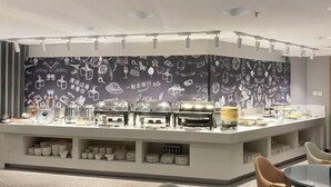 A modern breakfast bar with a variety of utensils and dishes, a patterned wall, and seating area. - Jiatai Chain Business Hotel (Zhuanghe High-speed Railway Station) (Zhuanghe)