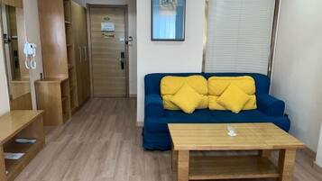 A room with a blue sofa, yellow cushions, a wooden table, and a wooden wardrobe.