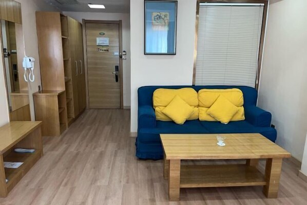 A room with a blue sofa, yellow cushions, a wooden table, and a wooden wardrobe. - Jiatai Chain Business Hotel (Zhuanghe High-speed Railway Station) (Zhuanghe)