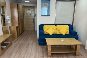 Una habitación con un sofá azul, cojines amarillos, una mesa de madera y un armario de madera.