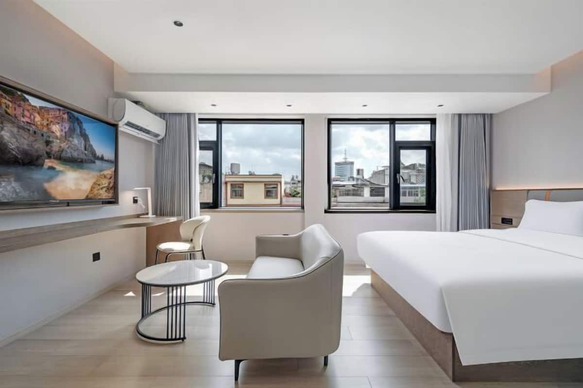 A modern hotel room with a large bed, a sofa, a small table, and a TV on the wall.