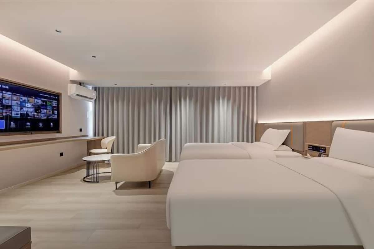 A modern hotel room with a large bed, a desk with a chair, a flat-screen TV, and a window with curtains.