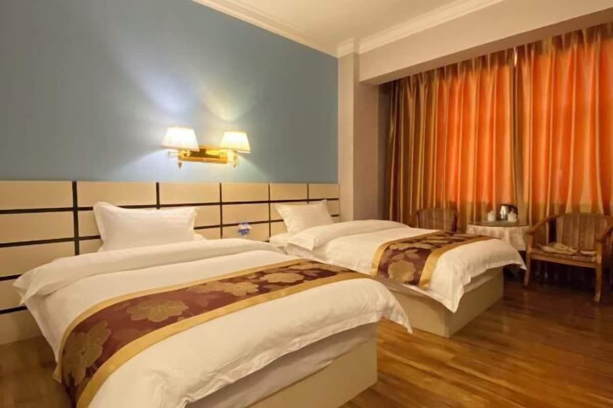 A hotel room with two beds, a nightstand, a lamp, and a chair.