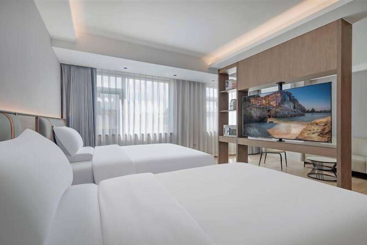 A hotel room with a large bed, a smaller bed, a TV on a wooden stand, a desk, and a chair.