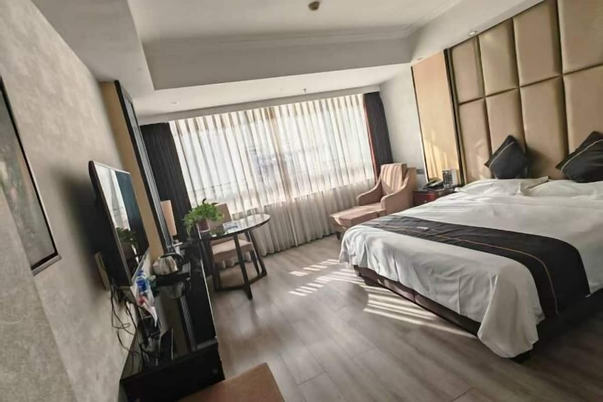 A hotel room with a bed, a desk with a chair, a small table, and a window with curtains.