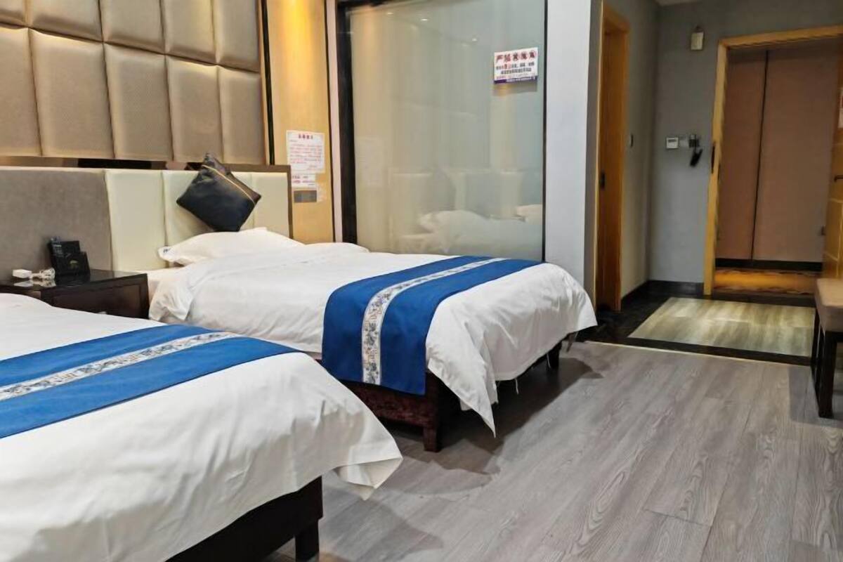 A hotel room with two beds, a wooden headboard, a glass partition, and a wooden door.