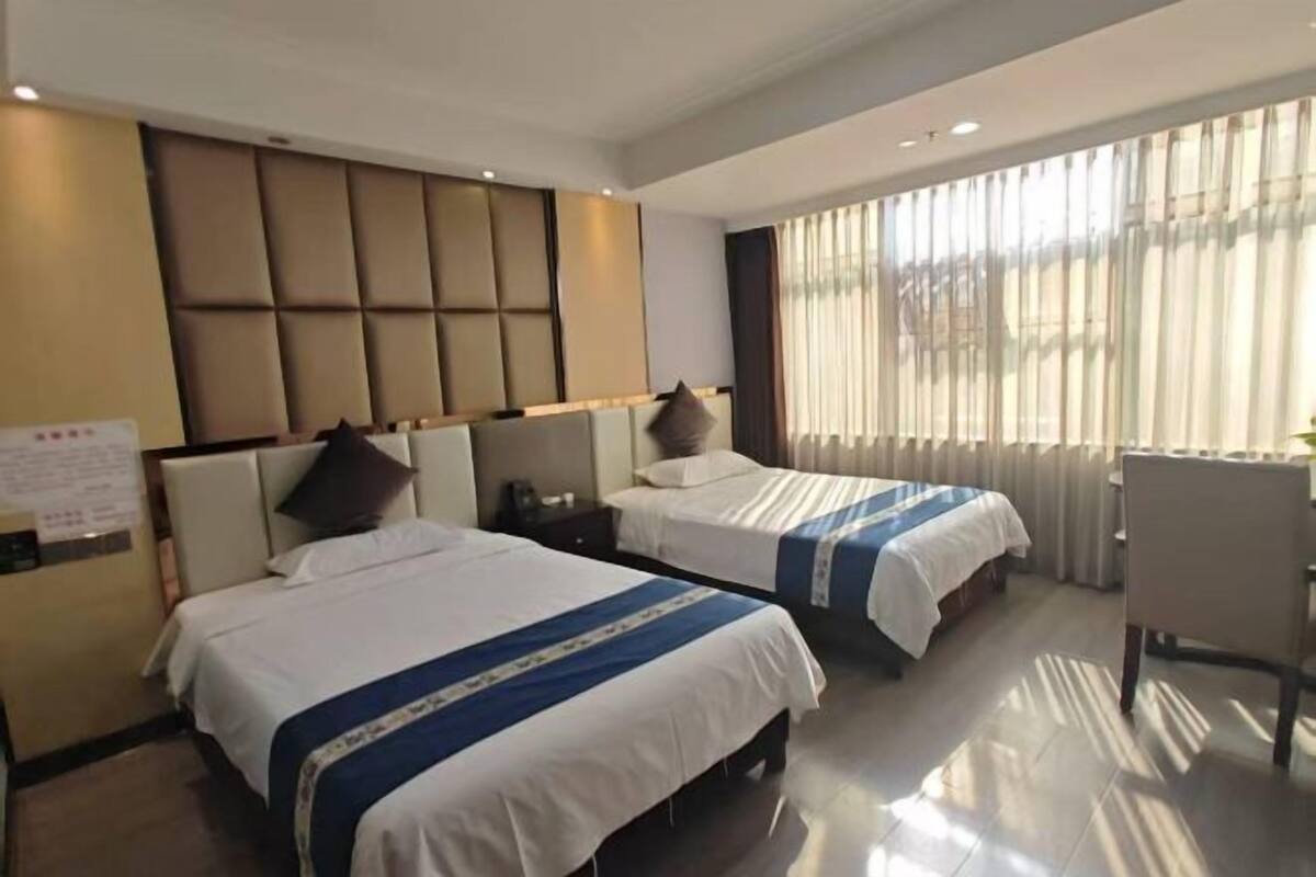 A hotel room with two beds, a desk, and a large window with curtains.