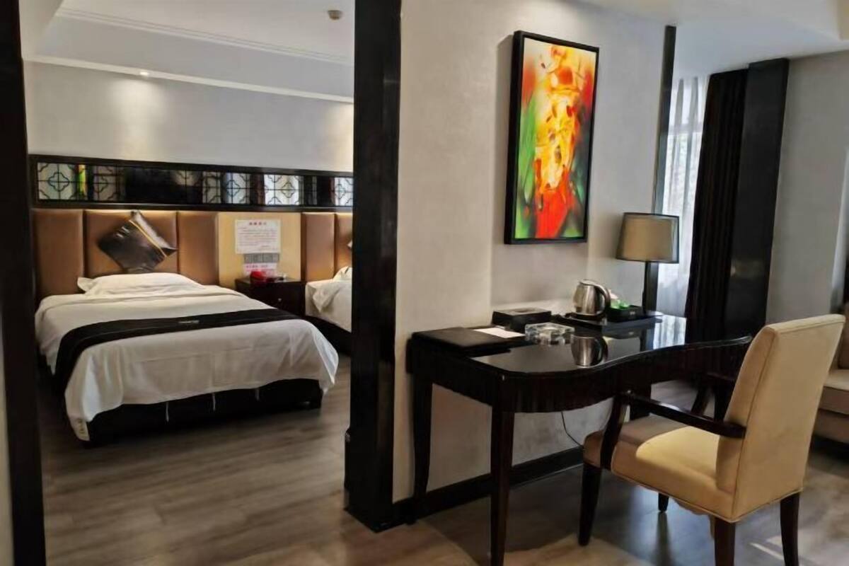 A hotel room with a bed, desk, chair, and a painting on the wall.