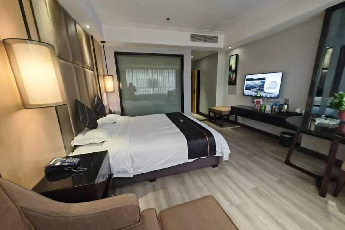 A hotel room with a bed, bedside table, lamp, TV, and a desk with a chair.
