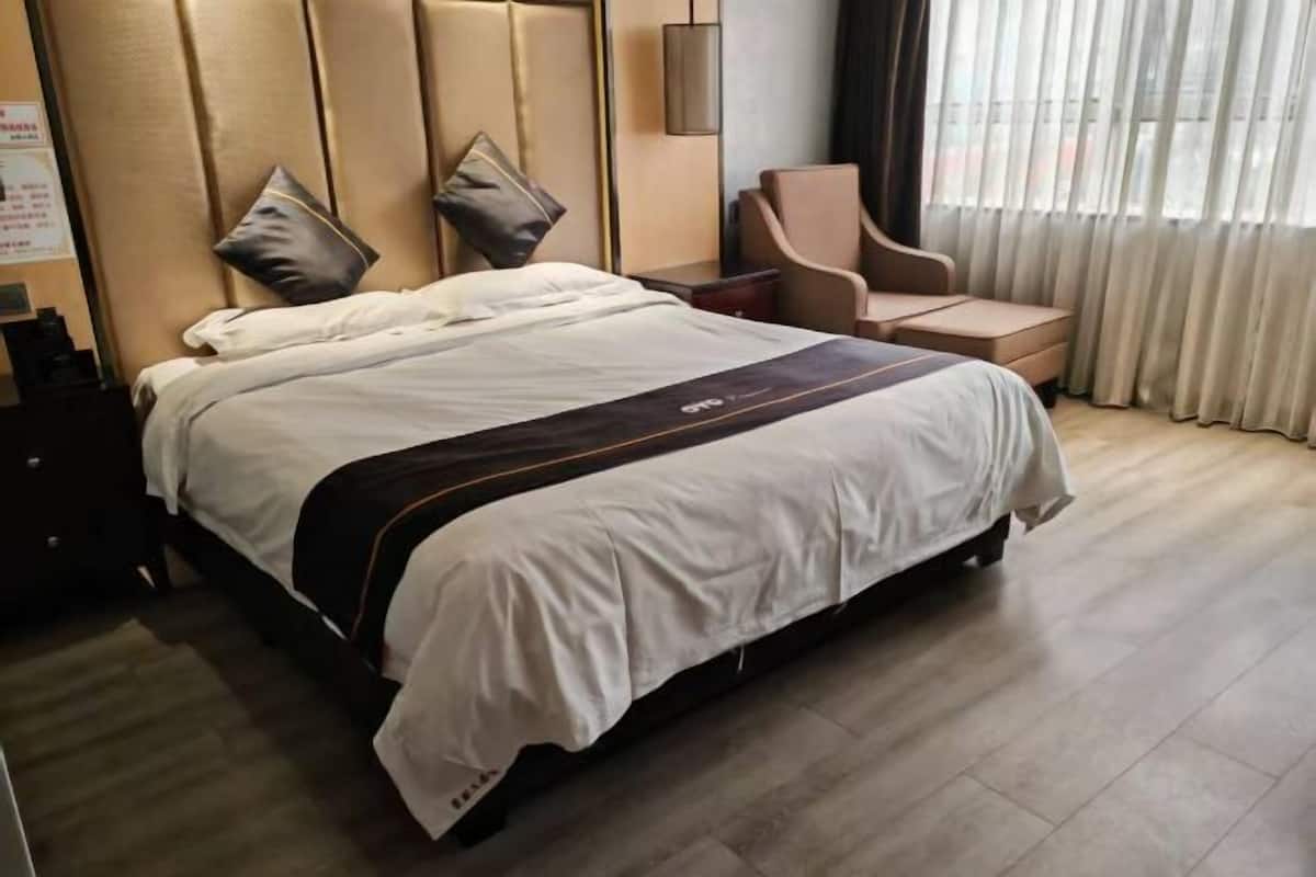 A hotel room with a large bed, a chair, a nightstand, and a window with curtains.