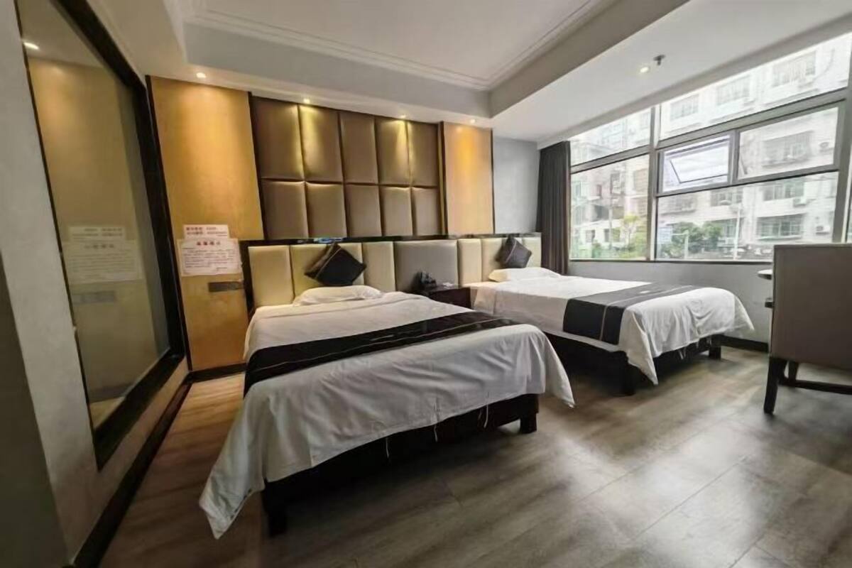 A hotel room with two beds, a large window, and a view of buildings outside.