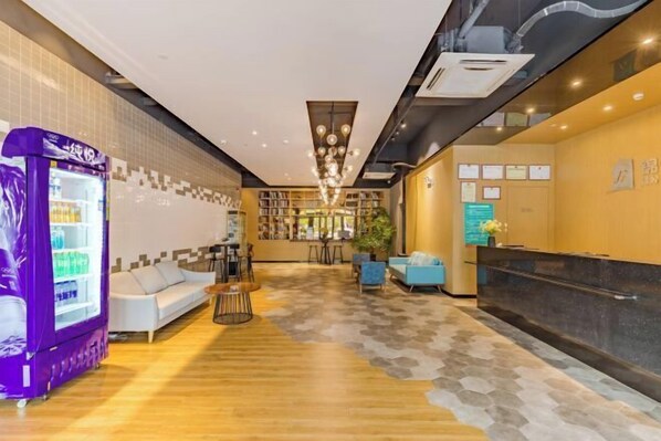 A hotel lobby with a reception desk, seating area, vending machine, and a patterned floor. - City Garden Hotel Chain (Chizhou Vocational College Xiushanmen Millennium Ancient City Building ) (Chizhou)