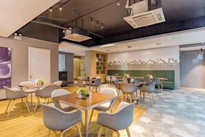 A modern conference room with round tables and chairs, a kitchen area, and a decorative wall. - City Garden Hotel Chain (Chizhou Vocational College Xiushanmen Millennium Ancient City Building ) (Chizhou)