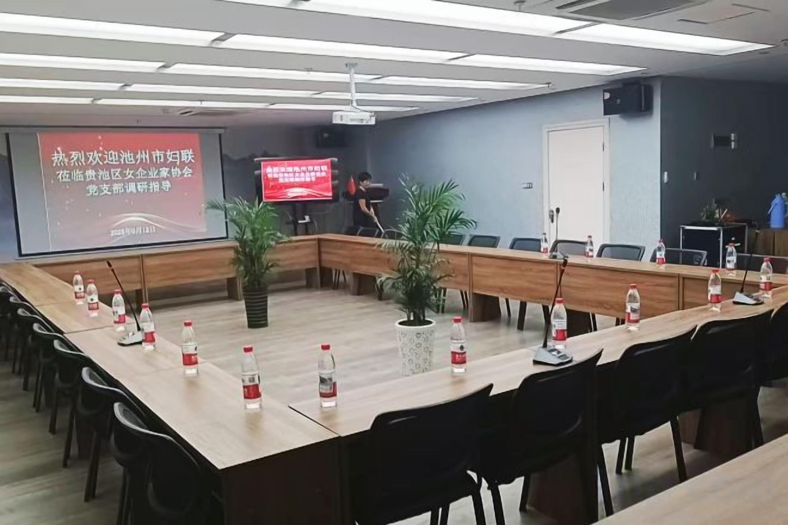 Un salón de conferencias con una larga mesa, sillas, una pantalla de proyector y un televisor.