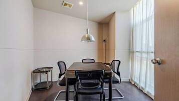 A conference room with a rectangular table, six chairs, a hanging light fixture, and a window with curtains.
